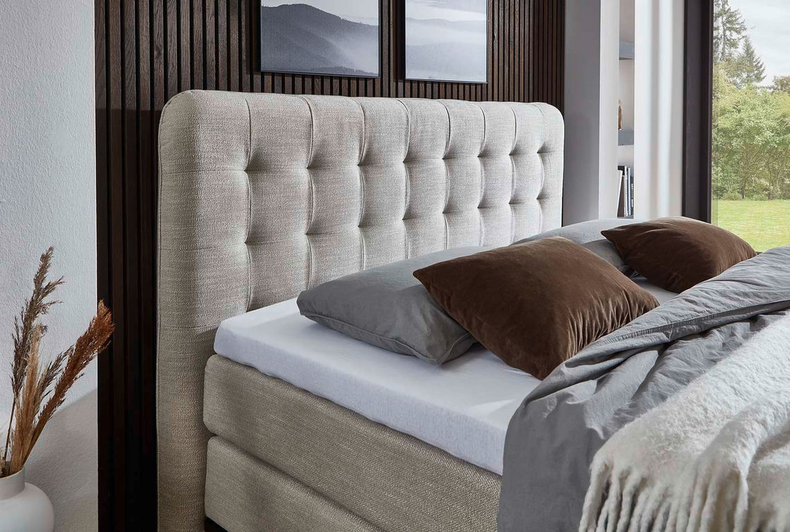 Boxspring — светлое стеганое изголовье кровати с коричневыми подушками.